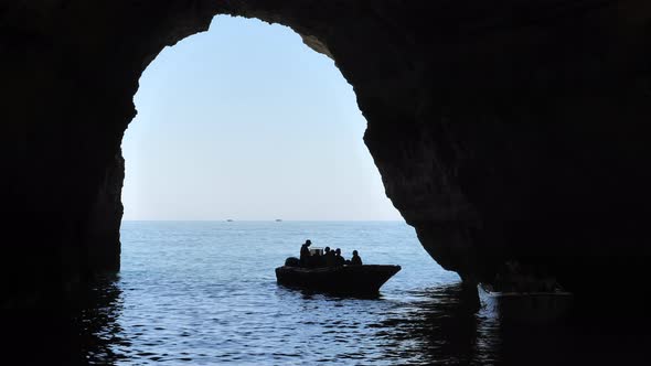 Silhouette of people on boat leaving sea cave. Static