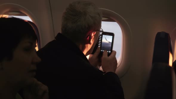 Unrecognizable Senior Male Passenger Taking Smartphone Photo of Plane Wing During Flight Sitting