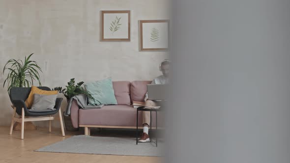 Man in Headphones Using Laptop on Sofa at Home