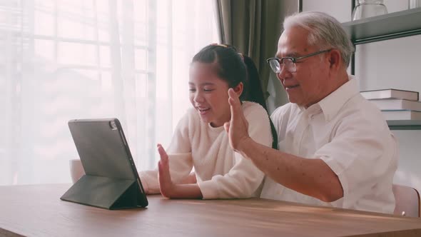 Happy senior man with little girl using a tablet on the table at home.