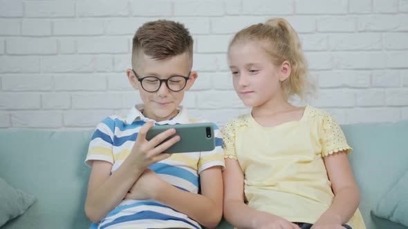 Close Up of an Excited Twins Kids Using Smartphone Sitting Together on Sofa