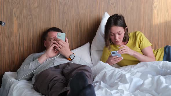 Man and Woman Surf Internet with Phones Lying on Hotel Bed