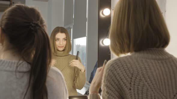 A Young Girl is Standing in Front of a Mirror and is Combing Her Long Hair and Doing a High Tail