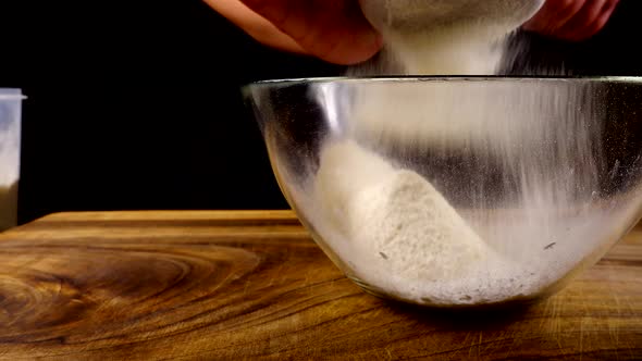 Sifting flour through a sieve into a glass bowl in the kitchen