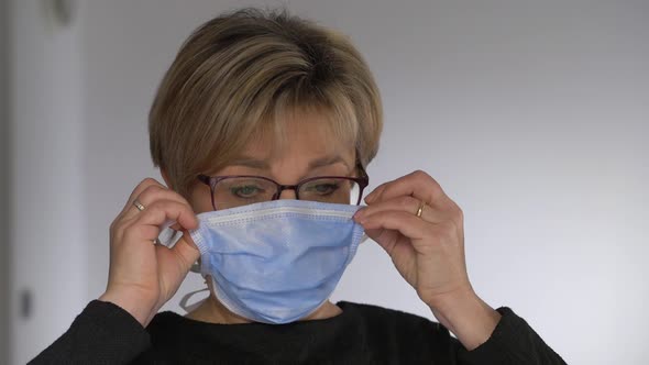 serious woman putting on the surgical mask looking at camera - corona virus