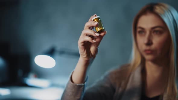 Woman Patient Looks at Remedy in Bottle in Semidark Room
