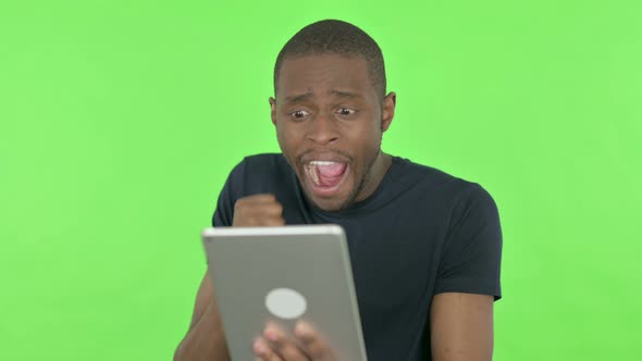 Young African Man Celebrating Success on Tablet on Green Background