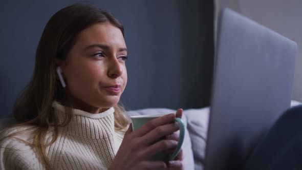 Woman drinking coffee while having a video chat on her laptop at home