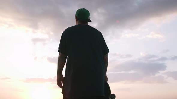 Young Man with Skateboard Looking on the Sea During Sunrise