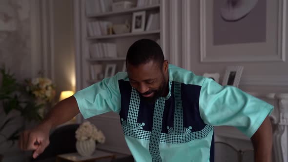 a Bearded AfricanAmerican Man in National Clothes Dances in a Living Room Against the Background of