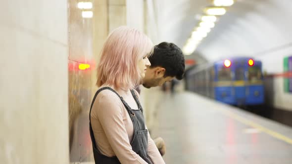 Side View Young Couple Sitting Indoors on Metro Station As Train Leaving in Slow Motion