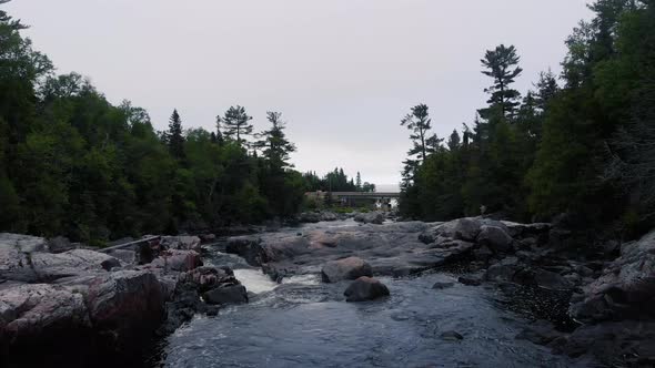 Flying low above the rocks down a river to a  bridge in the distance on a cloudy day, drone footage.