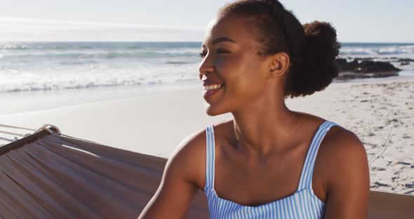 Close up of african american woman smiling while sitting on a hammock at the beach