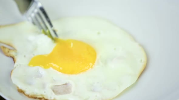 Eating sunny-side-up fresh farm egg with fork.