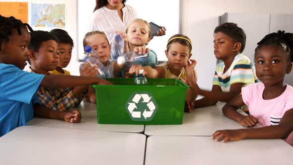 School kids putting waste bottles in recycle bin in classroom