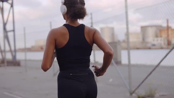 Young Woman In Sportswear And Headphones Jogging Along Harbour