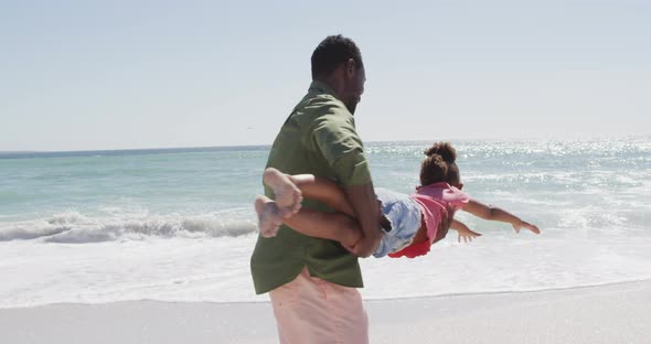 Smiling african american father with daughter playing on sunny beach