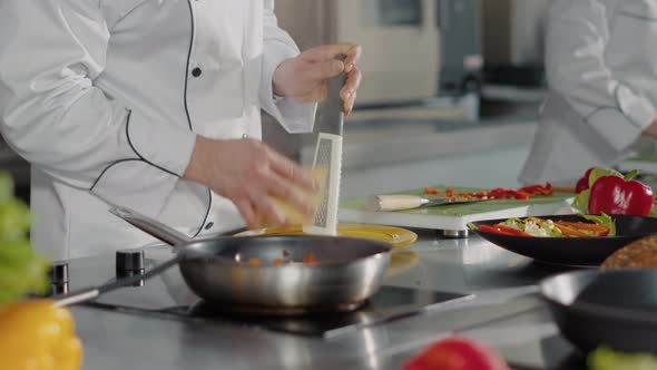 Professional Chef Using Grater to Add Shredded Cheese on Dish