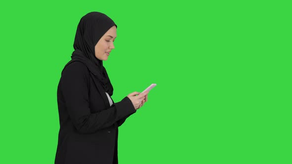 Muslim Woman Messaging on Her Mobile Phone While Walking on a Green Screen, Chroma Key.