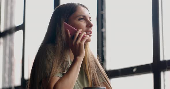 Pretty Woman Sitting in a Cafetalking on Mobile Phonesmiling and Looking Through the Window