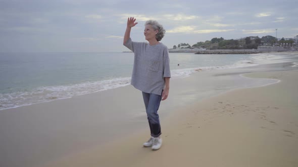 Happy Elderly Woman Wearing Casual Clothing and Sneakers Walking on Wet Sand and Seawaves