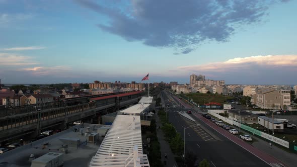 An aerial view over a strip mall roof between an elevated train station and a wide empty road. The c