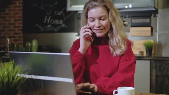 Girl working in kitchen. sitting typing on laptop talking on phone Home office