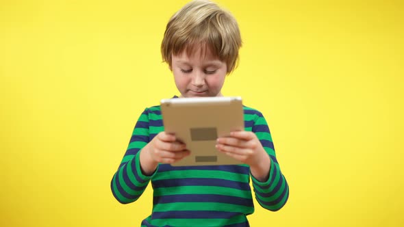 Middle Shot Portrait of Cute Boy Using Tablet Standing at Yellow Background