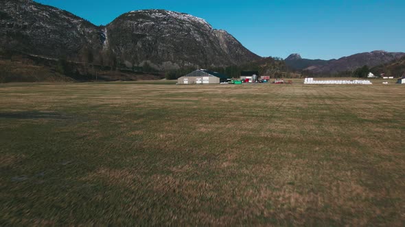 Drone Flight Towards Barn And Silo On Dairy Farm In Norway With Rocky Mountain In Background. wide