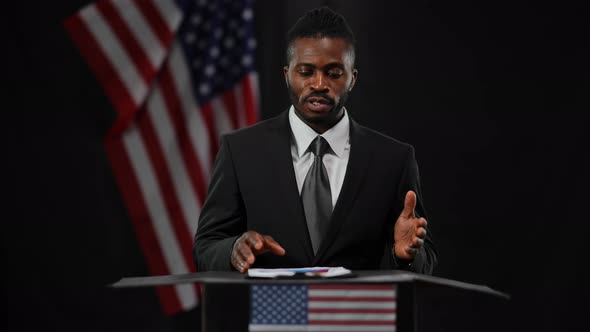 Serious African American Man in Elegant Formal Black Suit Speaking Gesturing Standing at Tribune