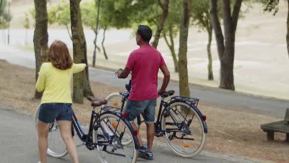 Back View of Caucasian Couple Walking with Bicycles in Park