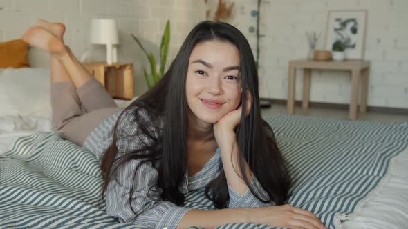 Slow Motion Portrait of Attractive Asian Woman Lying in Bed Smiling Looking at Camera at Home