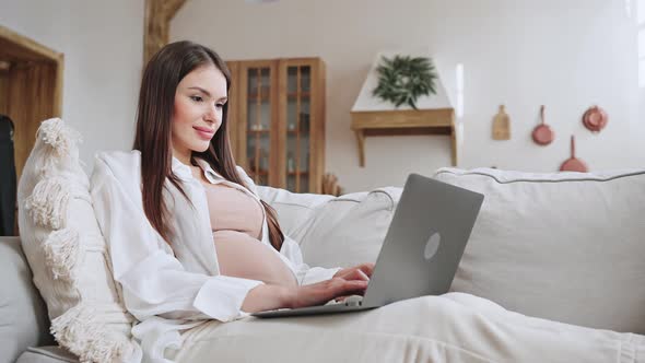 Pregnant Freelance Woman Lies on Sofa Writing Article