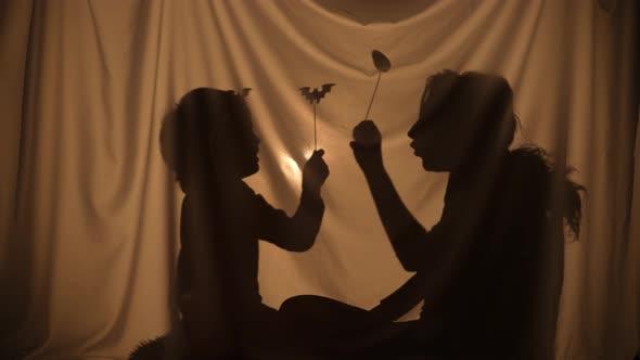 Unrecognizable Woman and Boy Telling Spooky Stories Using Shadow Play and Paper Bats and Pumpkins