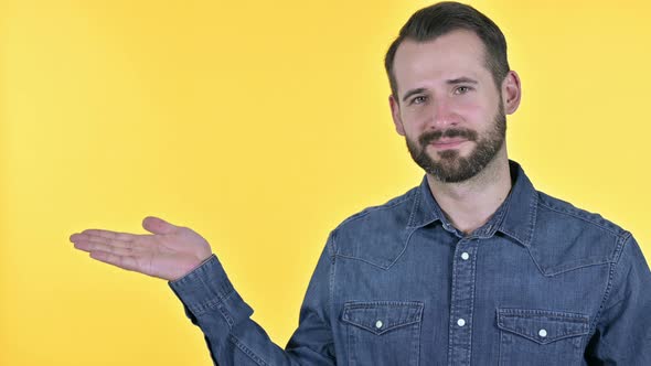 Beard Young Man Holding Product on Hand, Yellow Background