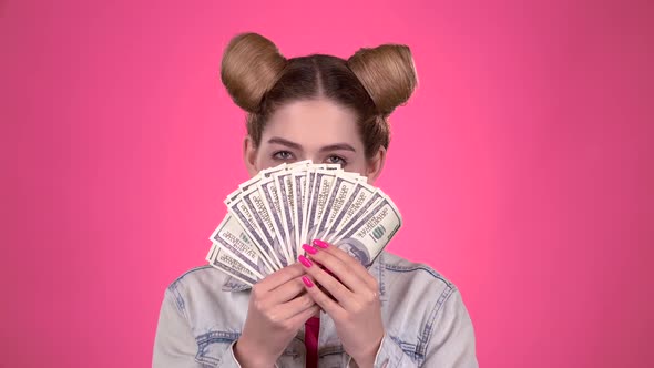 Girl Holds Paper Bills and Winks. Pink Background