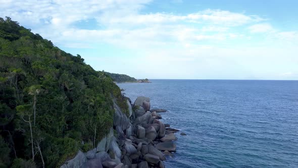 Aerial jib up shot of the rocky coastline with hills and vegetation near Bombinhas, Brazil