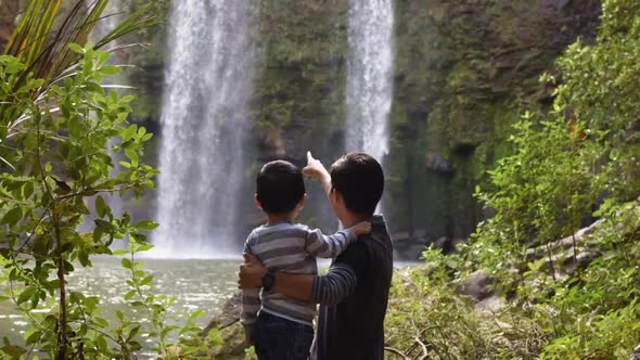 Cinemagraph of child in his father's arms looks at waterfalls. Zoom out