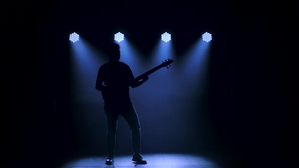 Silhouette of a Young Guy Playing on the Electric Guitar on Stage in a Dark Studio with Smoke and