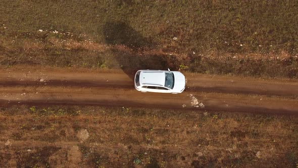 Drone Shoots From Above at a White Car Walking on a Rural Road in a Field