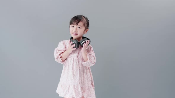 Girl with dress dancing and spinning with headphones in front of gray background.