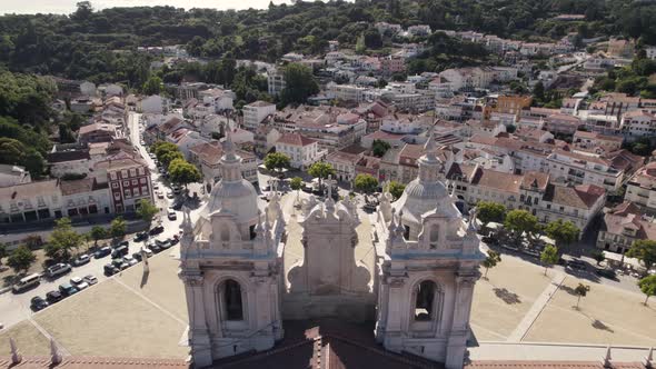 Fly over two striking church towers, Alcobaça Monastery, Portugal. Aerial forward towards the city