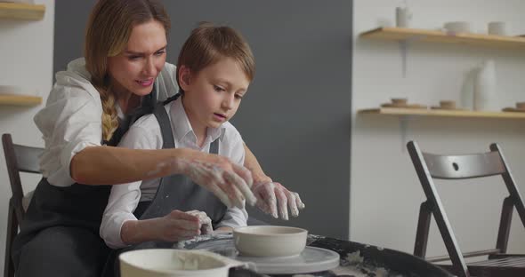 Mother and Kid Boy Working Together on Rotating Wheel in Pottery Workshop