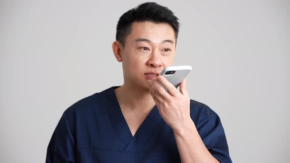 Smiling Asian doctor recording voice message by phone