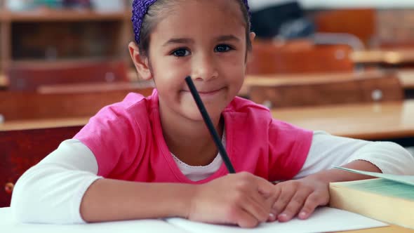 Cute Little Girl Colouring in Book in Classroom Smiling at Camera