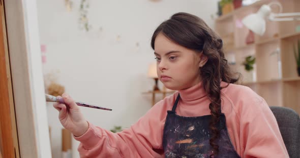 Close Up View of Cute Talanted Teenager Painting Picture While Sitting in Front of Molbert, Pretty