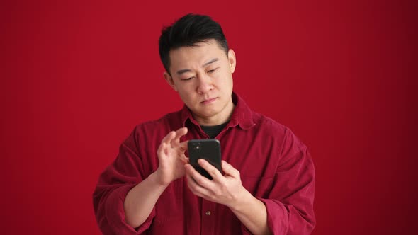 Serious Asian man wearing shirt texting by phone