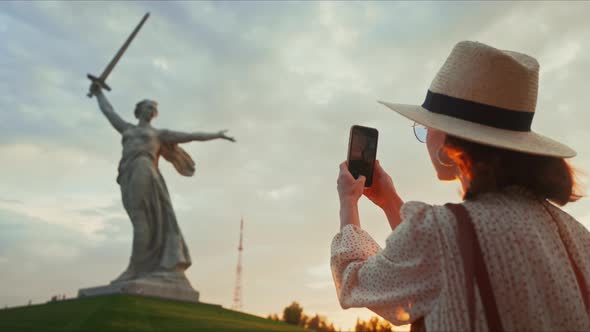 A young tourist in a hat taking a photo of the Motherland on a smartphone on the Mamayev Kurgan