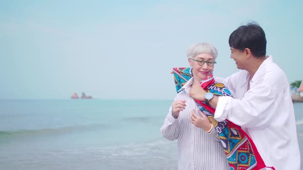 A senior man taking care to his partner while standing on the beach.