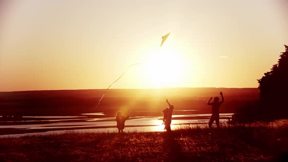 Young Family Standing on the Field While the Bright Orange Sunset - Father Playing with the Kite